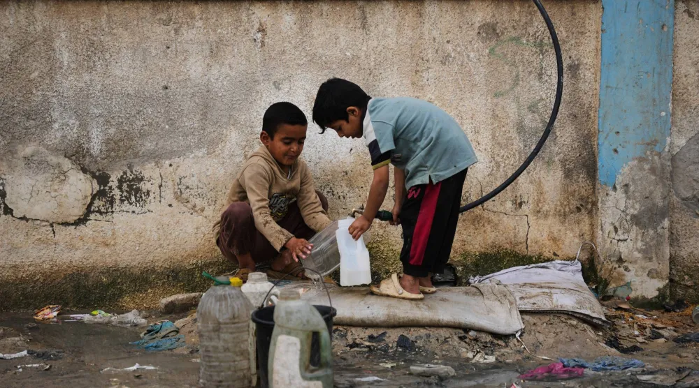أطفال فلسطينيون يملأون عبوات بالماء في مخيم للنازحين في دير البلح بقطاع غزة (أ.ب)
