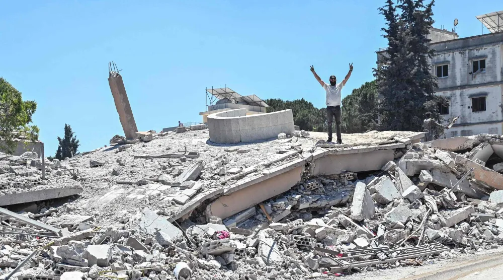 أحد سكان جنوب لبنان يرفع إشارة النصر بينما يقف فوق أنقاض منزله الذي دمرته غارات إسرائيلية (أ.ف.ب)