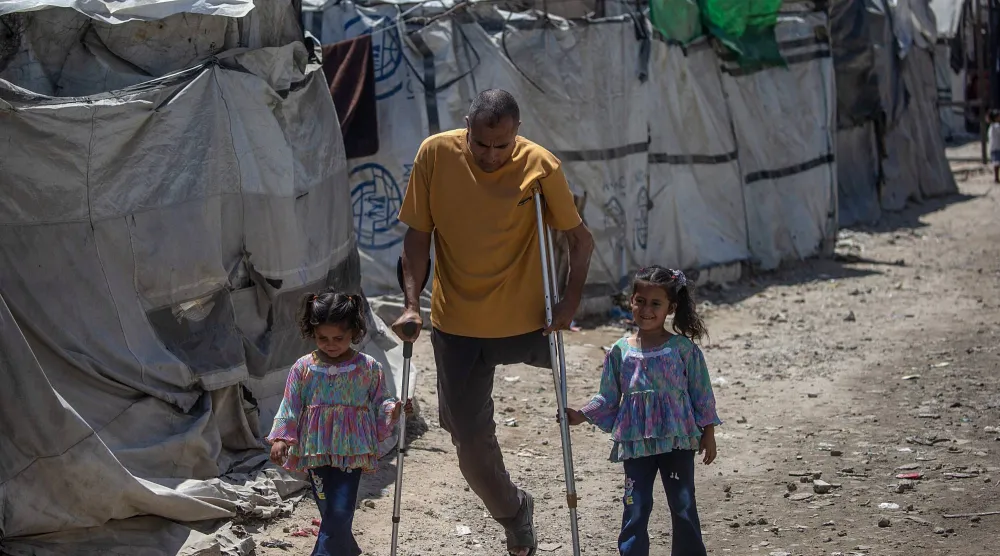 فلسطيني محرر من السجون الإسرائيلية مبتور الساق يسير مع ابنتيه في مخيم للنازحين بمدينة غزة (إ.ب.أ)