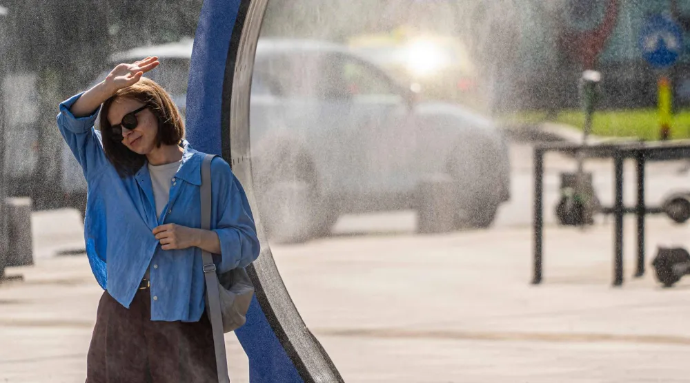 A woman cools off while walking through a water sprayer installed in central Bucharest, on June 28, 2026. (Photo by Mihai Barbu / AFP)