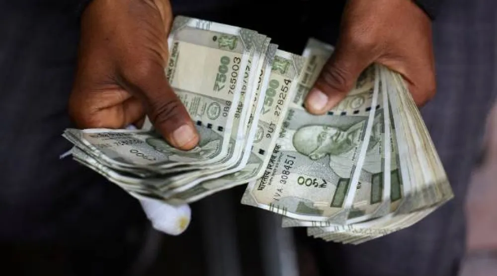 رجل يعدُّ أوراقاً نقدية هندية في كشك لصرافة العملات بأحد الأحياء القديمة في مدينة دلهي (رويترز)