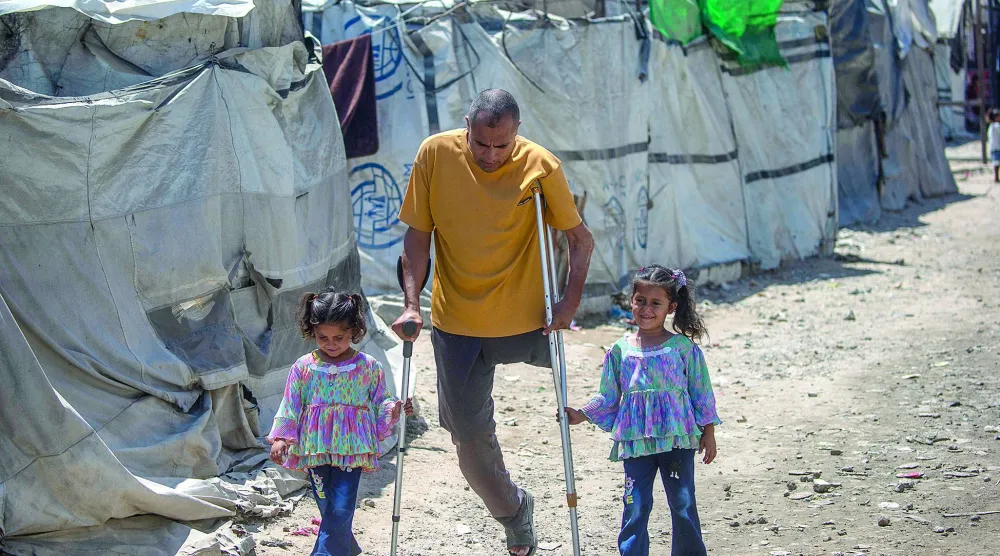 
فلسطيني محرَّر من السجون الإسرائيلية مبتور الساق يسير مع ابنتيه في مخيم للنازحين بمدينة غزة (إ.ب.أ)