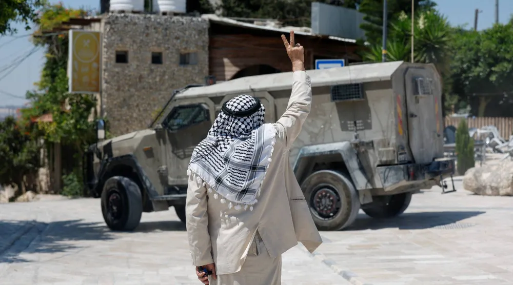 رجل فلسطيني يرفع إشارة النصر إلى جانب آلية عسكرية إسرائيلية، بينما يزور مستوطنون إسرائيليون وقوات من الجيش الإسرائيلي الموقع الأثري في سبسطية بالضفة الغربية المحتلة (رويترز)