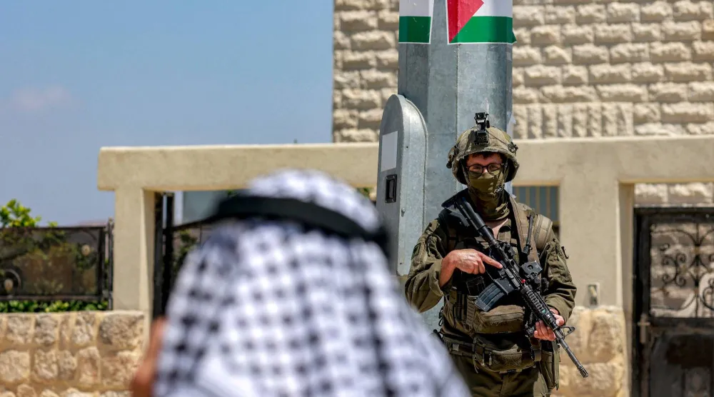 فلسطيني يتحدث عبر الهاتف بالقرب من جندي إسرائيل في موقع أثري بسبسطية شمال نابلس بالضفة الغربية المحتلة يوم الاثنين (أ.ف.ب)