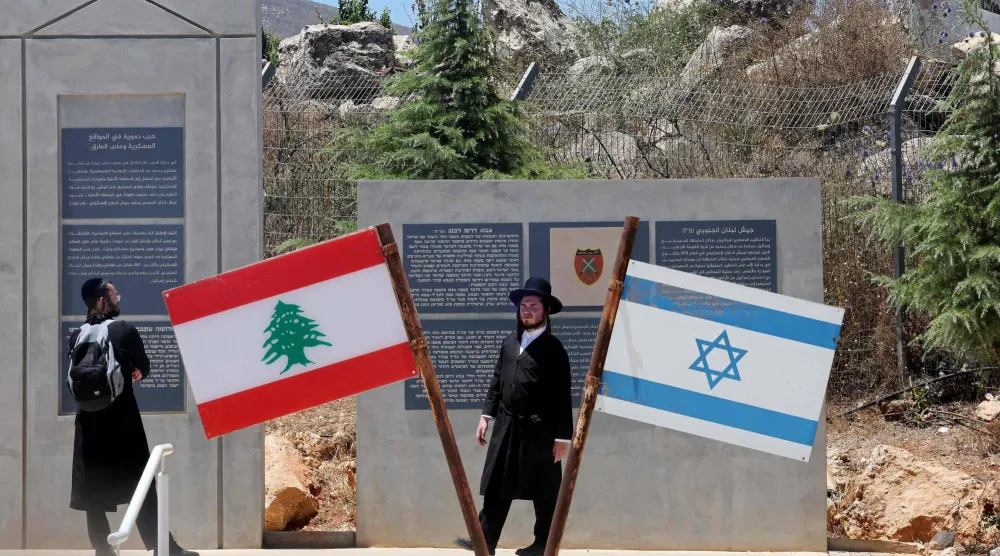 يهودان من طائفة «الحريديم» (المتشددين دينياً) يقفان بجوار العلمين الإسرائيلي واللبناني في موقع عند الحدود مع لبنان في شمال إسرائيل (أ.ف.ب)