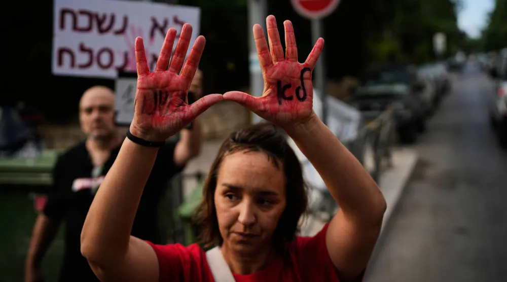 سيدة ترفع يديها المصبوغتين باللون الأحمر خلال احتجاج أمام مقر إقامة رئيس الوزراء الإسرائيلي في القدس الخميس (أ.ب)