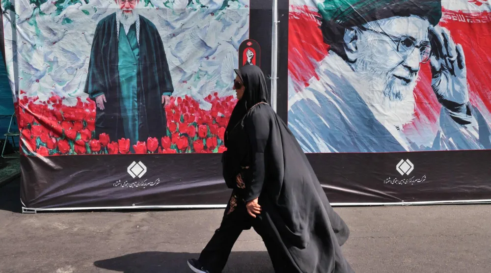 امرأة تمر أمام لوحة إعلانية تحمل صورة المرشد الإيراني الراحل علي خامنئي بينما يتجمع المشيعون في المصلى الكبير لإلقاء النظرة الأخيرة عليه في بداية مراسم جنازته في طهران (أ.ف.ب)