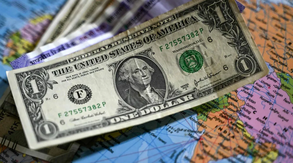 ورقة نقدية من فئة الدولار موضوعة فوق أوراق نقدية من فئة الروبية الهندية على خريطة العالم (أ.ف.ب)