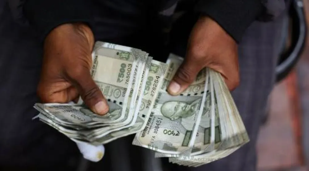 رجل يعدّ أوراقاً نقدية هندية في كشكٍ لتبديل العملات على جانب الطريق بالأحياء القديمة بمدينة دلهي (رويترز)