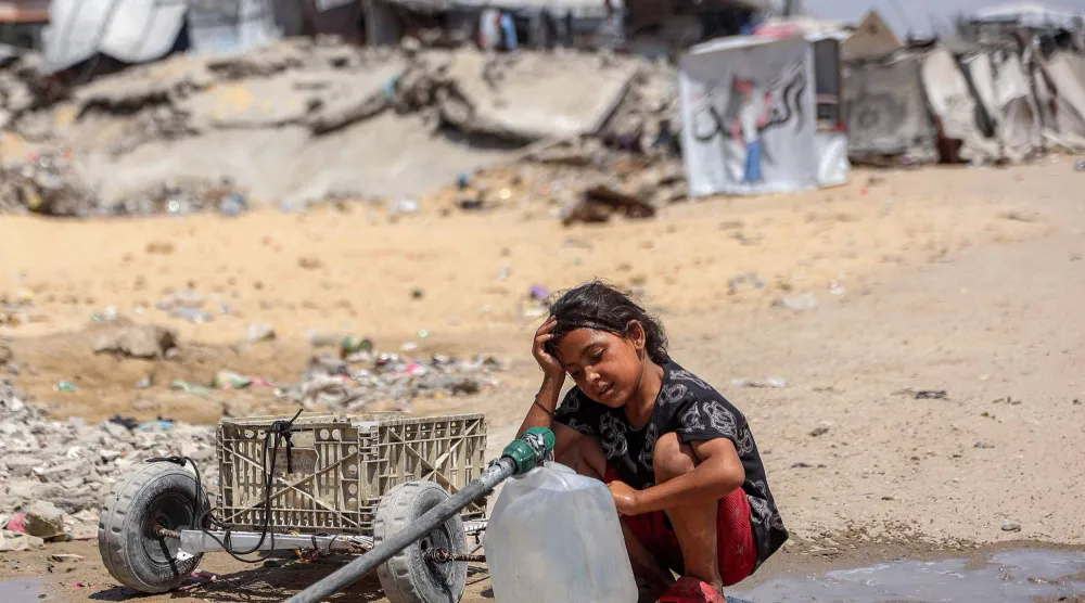 فتاة فلسطينية تملأ أوعيةً بالماء المستخرج من بقايا أنابيب تحت الأرض بمخيم للنازحين جراء الحرب في حي الشيخ رضوان بمدينة غزة (أ.ف.ب)
