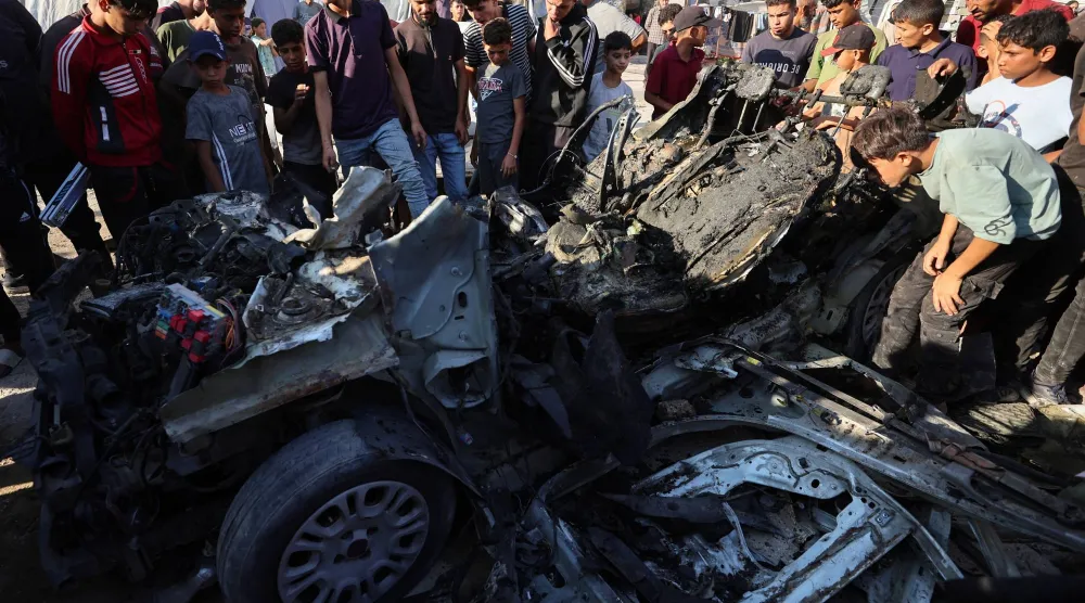 فلسطينيون يتفقدون موقع غارة إسرائيلية استهدفت مركبة في مدينة غزة (رويترز)