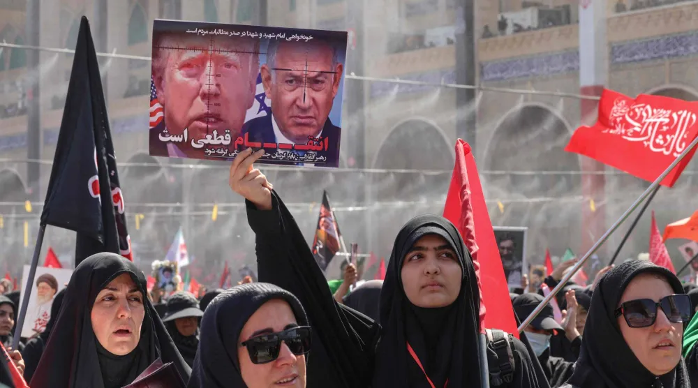 يرفع أحد المشيعين لافتة تحمل صورتي الرئيس ترمب ورئيس الوزراء الإسرائيلي بنيامين نتنياهو مع عبارة «الانتقام حتمي» (أ.ف.ب)