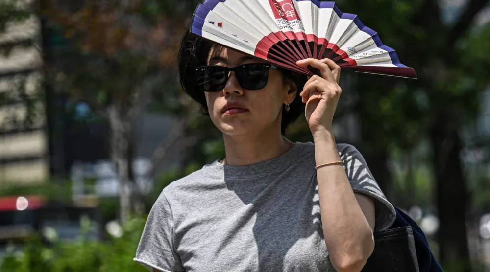 A woman uses a fan to shelter from the sun on a street in Seoul on July 12, 2026. (Photo by JADE GAO / AFP)