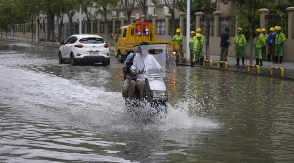  شبان يركبون دراجة كهربائية صغيرة عبر شارع غمرته المياه بعد مرور إعصار بافي في يويتشينغ بونتشو بمقاطعة تشجيانغ بالصين (إ.ب.أ)