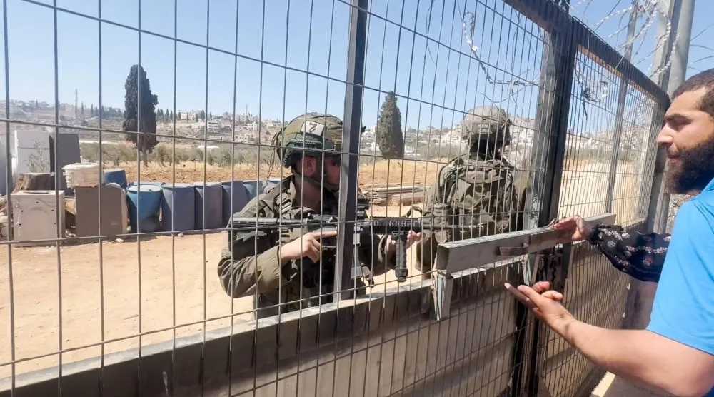 أحد عناصر القوات الإسرائيلية يتحدث إلى فلسطيني بينما يصوب سلاحاً باتجاهه في قرية المغير قرب رام الله (رويترز)