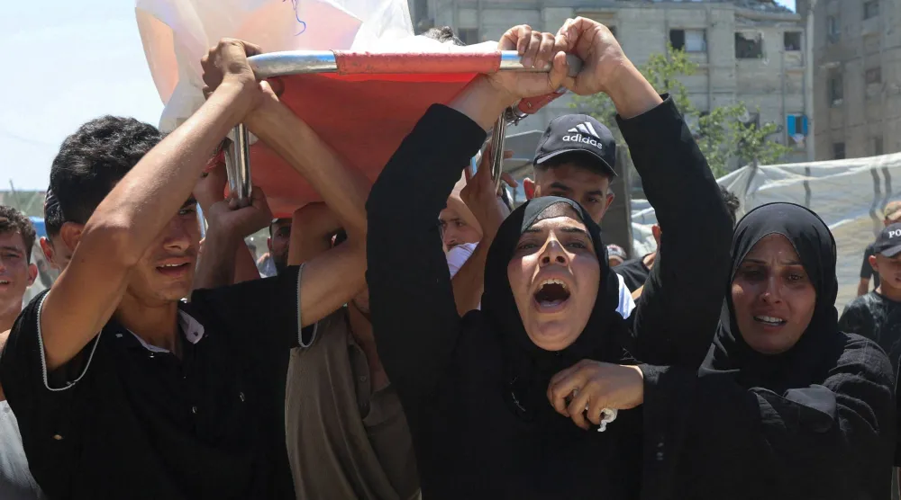 والدة الطفل الفلسطيني معتز أبو شعر الذي قُتل بنيران إسرائيلية ومشيعون يحملون جثمانه في خان يونس جنوب غزة يوم الثلاثاء (رويترز)
