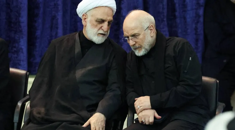 رئيس السلطة القضائية غلام حسين محسني إجئي يهمس في أذن قاليباف على هامش مراسم تأبين المرشد السابق علي خامنئي مساء الثلاثاء (البرلمان الإيراني)