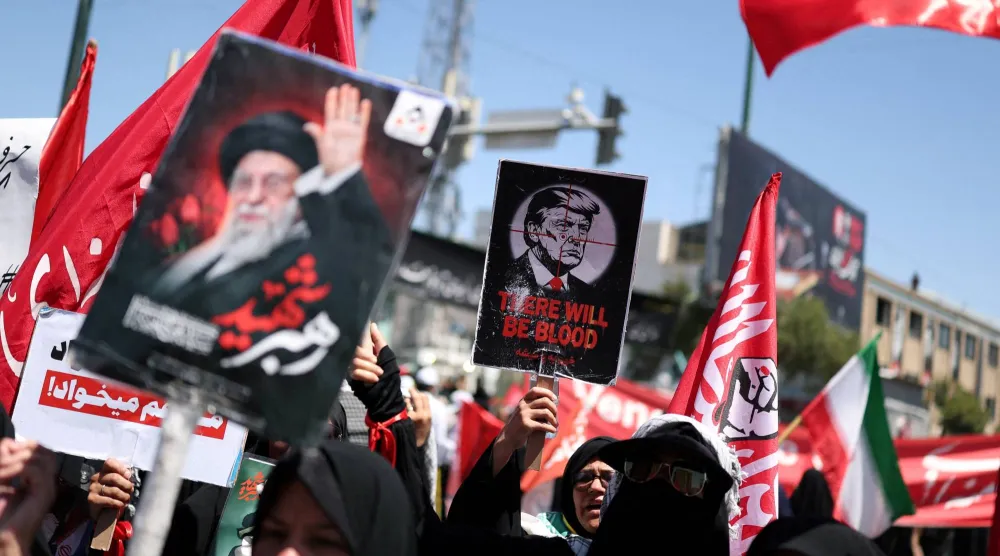 امرأة تحمل لافتة مناهضة للرئيس الأميركي دونالد ترمب بينما يتجمّع المشيّعون في يوم دفن المرشد الإيراني علي خامنئي... في مشهد بإيران يوم 9 يوليو 2026 (رويترز)