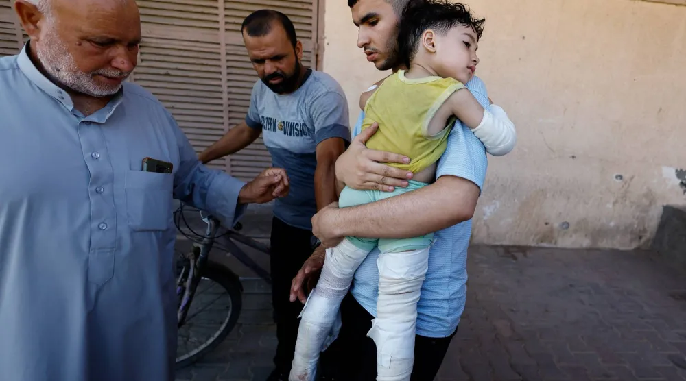 فلسطيني يحمل طفلاً أصيب بغارة إسرائيلية قتلت والديه في مستشفى «شهداء الأقصى» بدير البلح وسط قطاع غزة الأربعاء (رويترز)