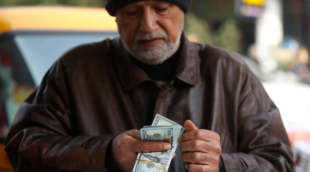 رجل يعدّ أوراقاً نقدية من فئة الدولار الأميركي في سوق الكفاح ببغداد في 27 ديسمبر 2022 (أ.ف.ب)