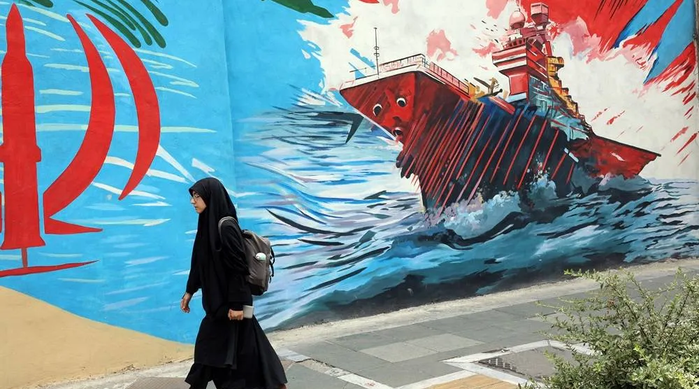 A woman walks next to anti-US graffiti on a street in Tehran, Iran, 20 July 2026. (EPA)