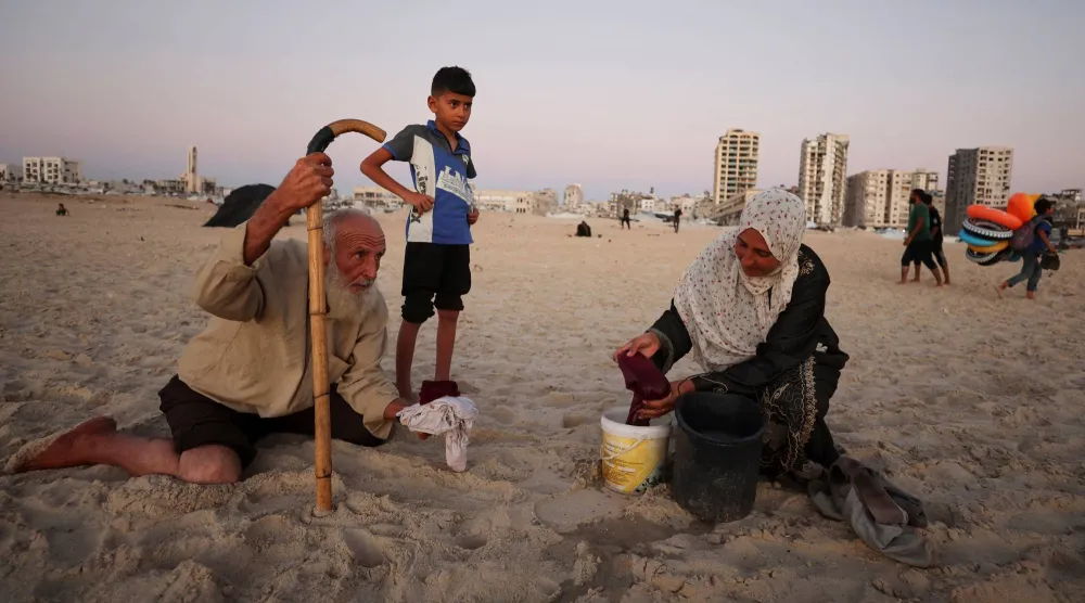 امرأة فلسطينية نازحة تغسل ملابسها على شاطئ البحر الأبيض المتوسط ​​في مدينة غزة (رويترز)