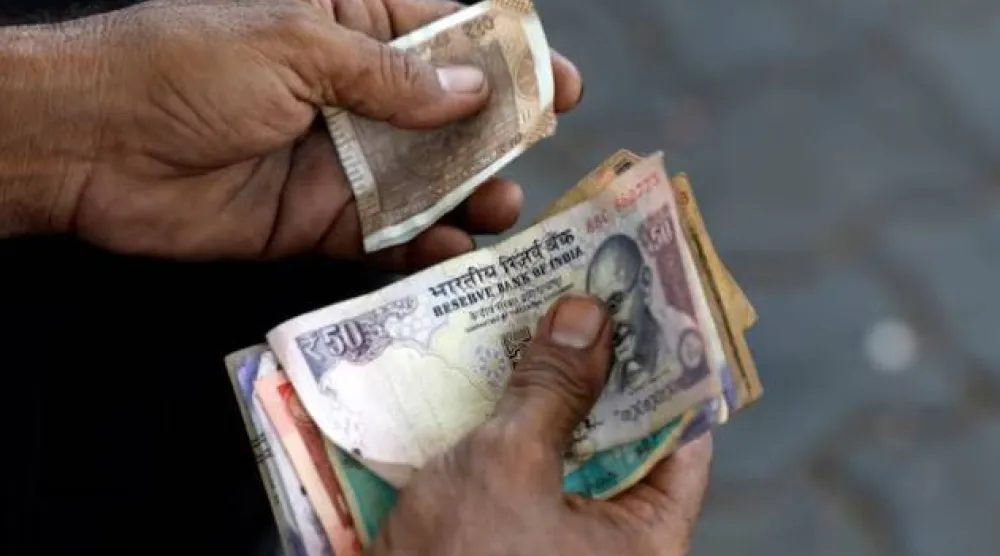 أمين صندوق يمسك أوراقاً نقدية هندية في محطة وقود بمدينة أحمد آباد (رويترز)
