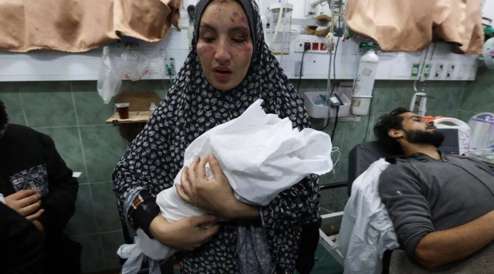 سيدة فلسطينية مصابة تحمل طفلها حديث الولادة بأحد مستشفيات غزة (رويترز)