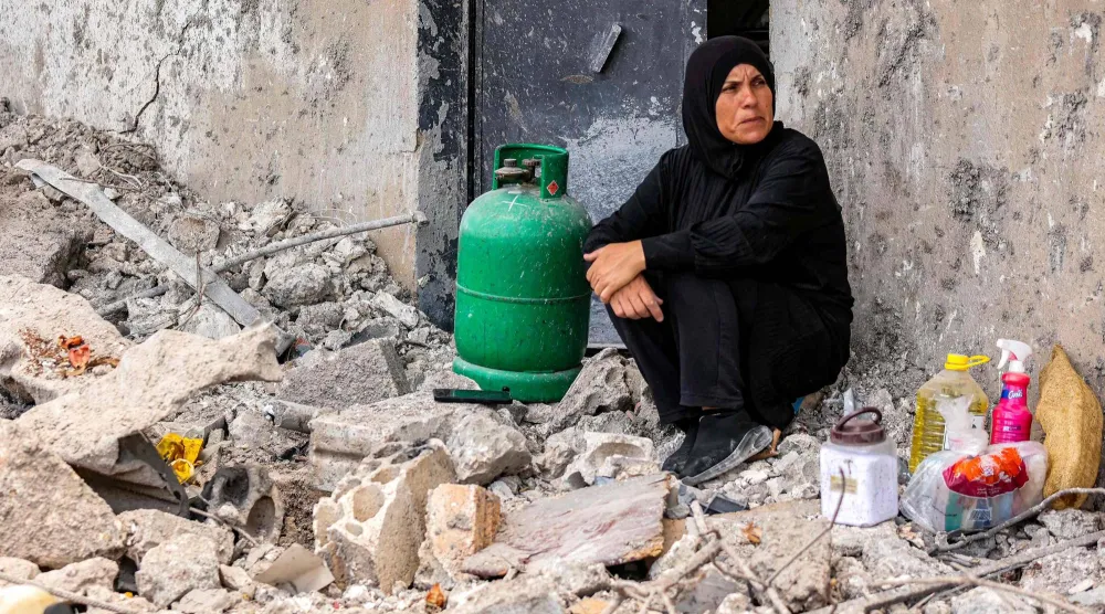 سيدة تجلس إلى جانب جرّة غاز عند باب منزلها المدمر نتيجة القصف الإسرائيلي في بلدة زوطر الغربية بجنوب لبنان (أ.ف.ب)
