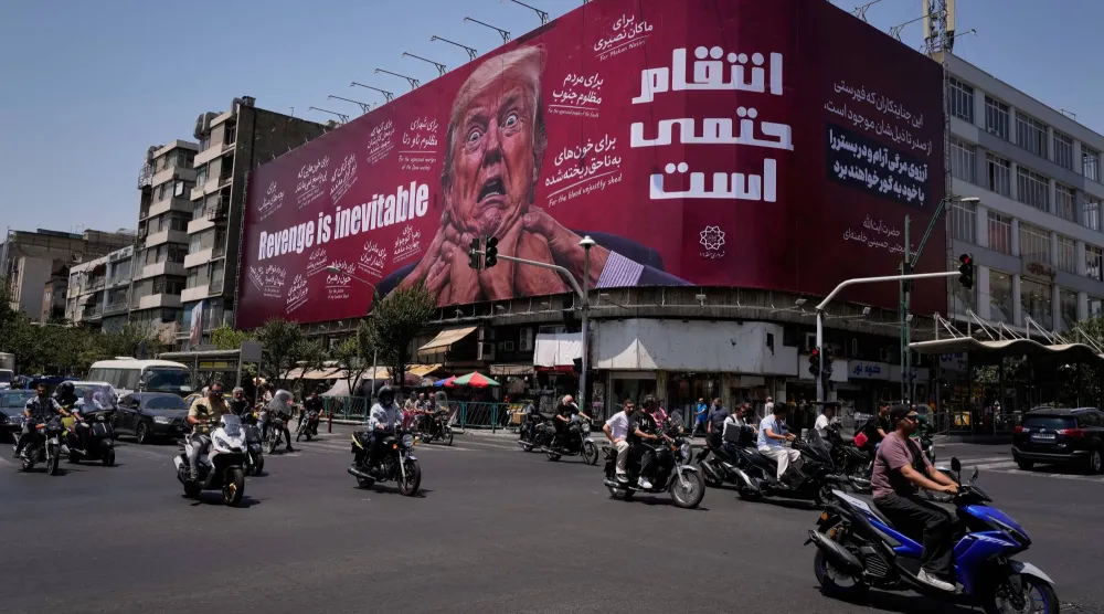 مارة في شارع أمام لوحة إعلانية في طهران تظهر الرئيس الأميركي دونالد ترمب مع عبارة بالإنجليزية والفارسية تقول: «الانتقام حتمي»، 27 يوليو 2026 (أسوشييتد برس)