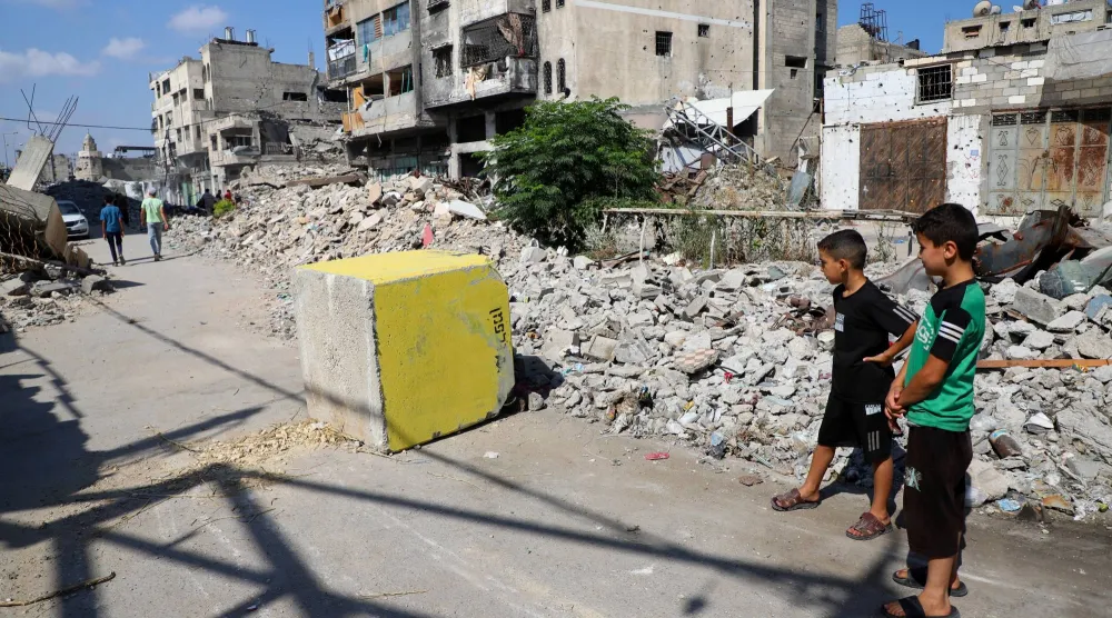 فتيان فلسطينيون ينظرون إلى كتلة خرسانية صفراء تُشير إلى «المنطقة الصفراء» الخاضعة للسيطرة العسكرية الإسرائيلية في حي طفاح بمدينة غزة (رويترز)
