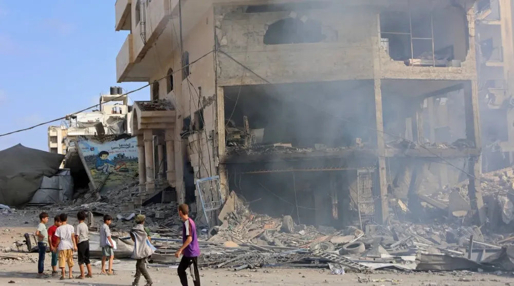 İsrail'in Gazze şehrine düzenlediği hava saldırısının ardından El-Calaa Caddesi'nde yıkılmış bir binanın yanında duran Filistinli çocuklar (AFP)