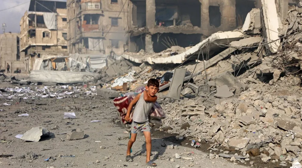 صبي فلسطيني يحمل لحافاً يسير بمحاذاة مبانٍ مدمرة في شارع الجلاء عقب غارة إسرائيلية بغزة (أ.ف.ب)