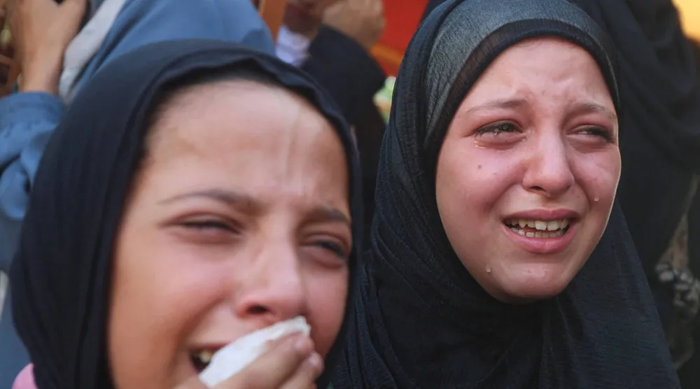 فتاتان تنتحبان خلال جنازة فلسطينيين قُتلوا في غارات إسرائيلية استهدفت خياماً في خان يونس جنوب غزة (رويترز)