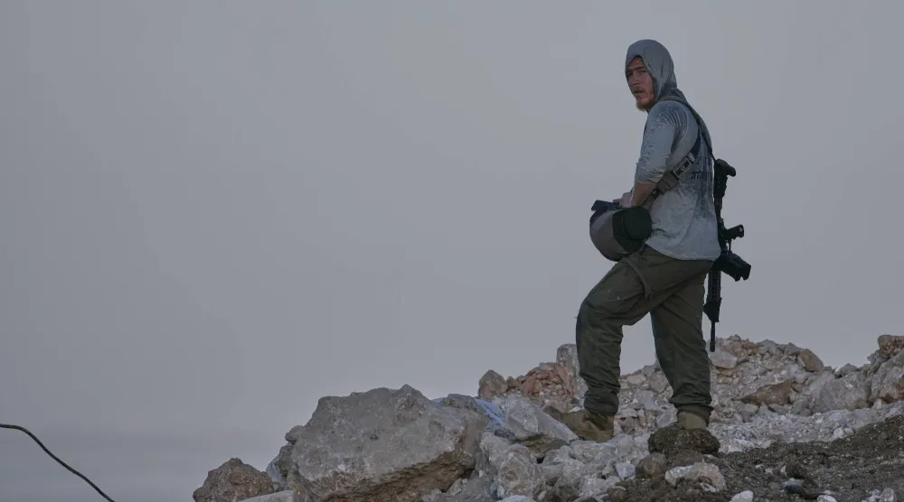 مستوطن إسرائيلي مسلح يقف على سفح مطل على بلدة تل الفلسطينية قرب رام الله الضفة الغربية يوم الجمعة (أ.ب)