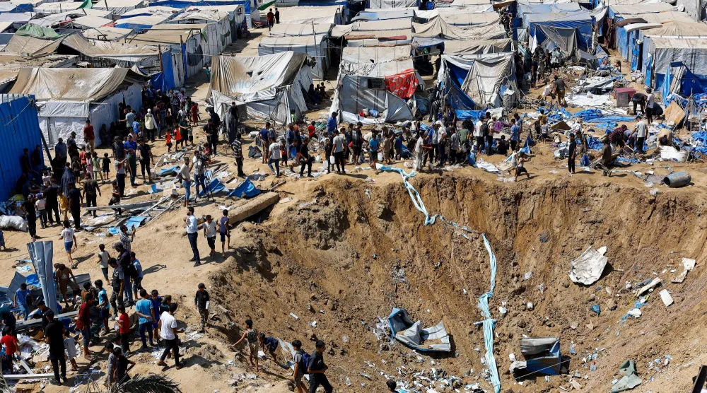 فلسطينيون في موقع ضربة إسرائيلية على مستودع للأدوية قرب خيام للنازحين في دير البلح أمس (رويترز)