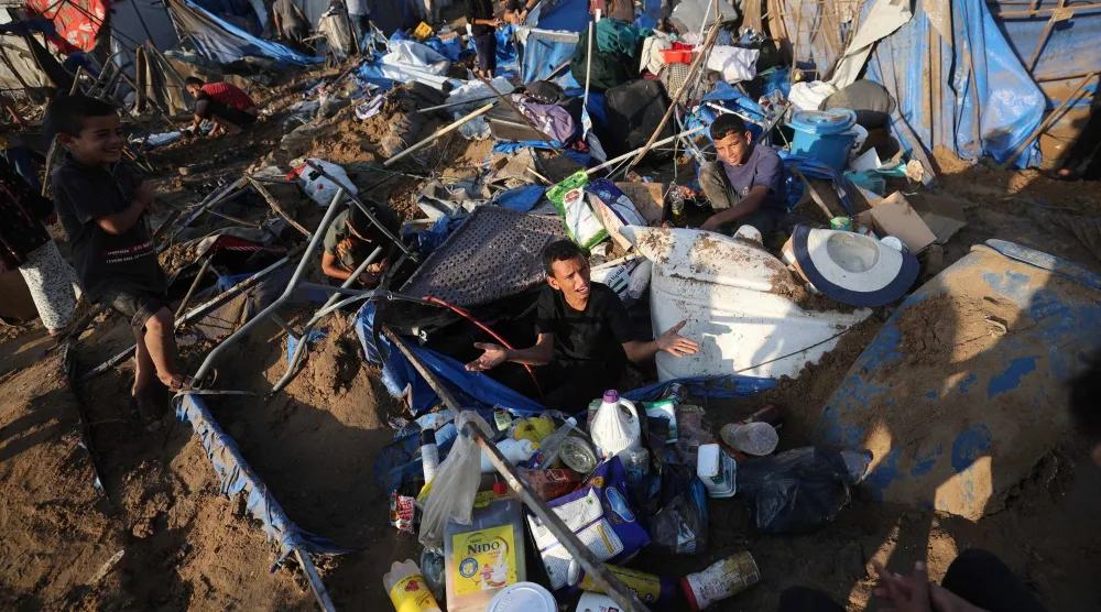 نازح فلسطيني يجلس على الرمال بين بقايا خيمته التي دُمّرت عقب غارة جوية إسرائيلية استهدفت مستودعاً للإمدادات والمستلزمات الطبية والأدوية بالقرب من مستشفى شهداء الأقصى في مدينة دير البلح وسط قطاع غزة في الأول من أغسطس الحالي (أ.ف.ب)