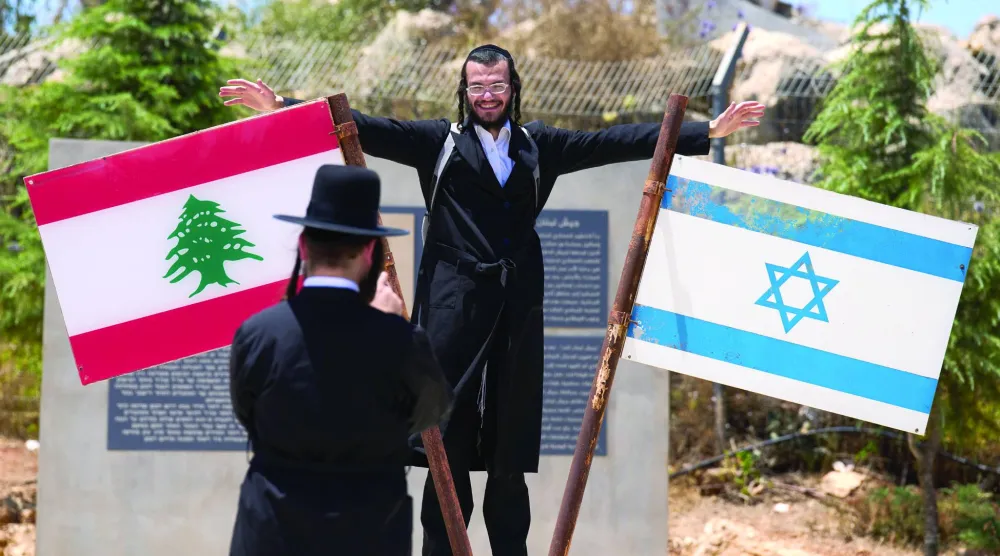 إسرائيلي متشدد يلتقط صورة قرب عَلَمَي لبنان وإسرائيل مرفوعين على نصب تذكاري في بلدة المطلة المحاذية للحدود اللبنانية (أرشيفية - أ.ب)