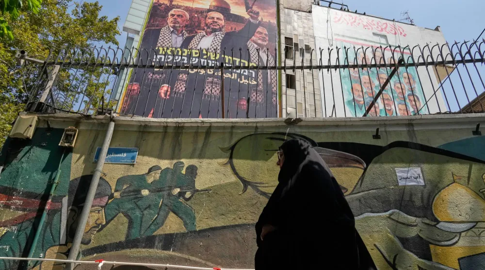 إيرانية تسير أمام لوحة في طهران تحمل صور خليل الحية زعيم «حماس» الحالي مع إسماعيل هنية ويحيى السنوار زعيمي الحركة السابقين اللذين قتلتهما إسرائيل (أ.ب)