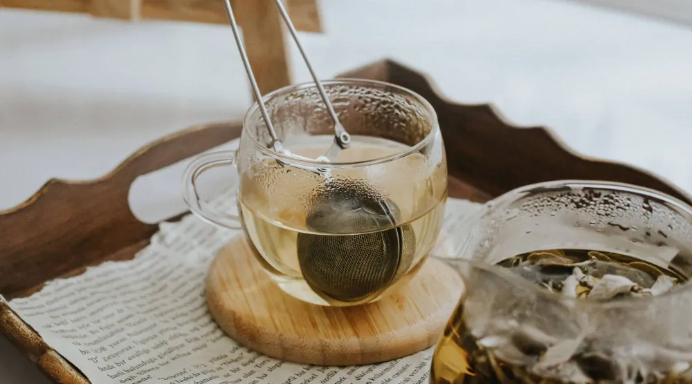 كوب شاي دافىء مع مصفاة يظهر على صينية من خشب (بيكسلز)