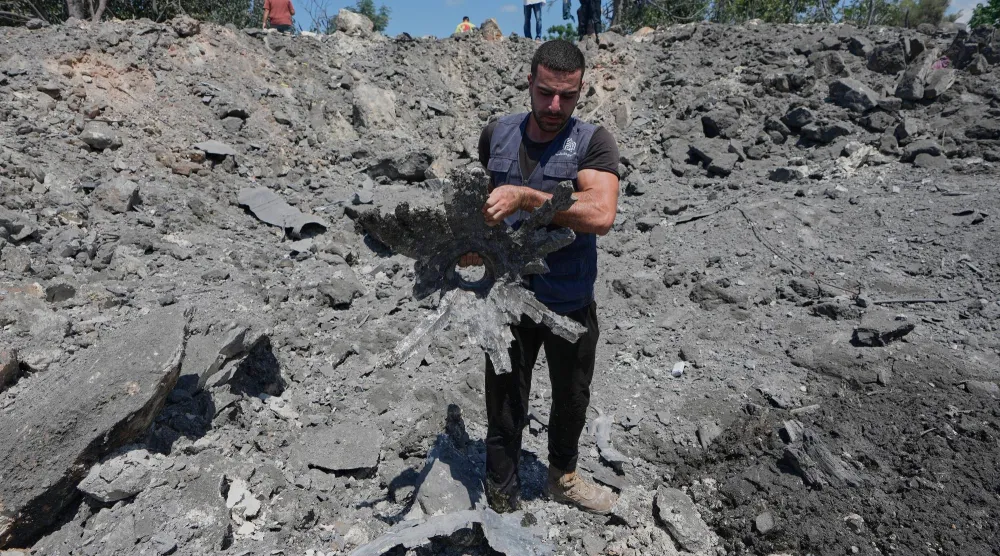 A Lebanese man holds a piece of shrapnel as he stands in a crater caused by an Israeli airstrike in the village of Burj al-Shamali, southern Lebanon, Thursday, Aug. 6, 2026. (AP Photo/Mohammed Zaatari)