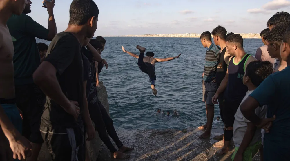 فلسطينيون يراقبون شاباً يقفز إلى البحر في خان يونس جنوب قطاع غزة يوم الجمعة (إ.ب.أ)