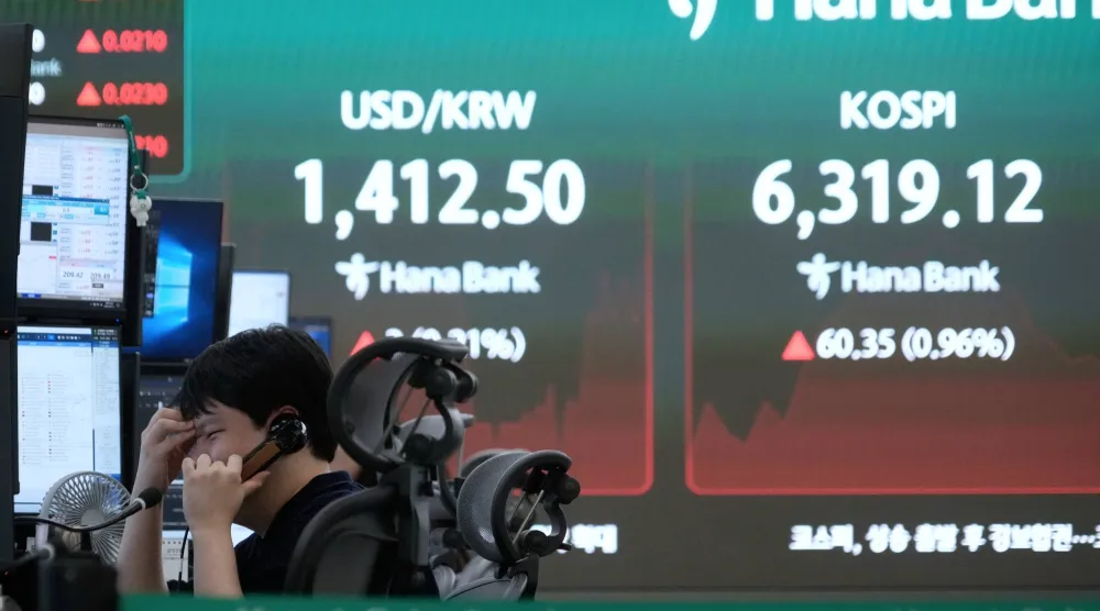 متداول عملات بالقرب من شاشة تعرض مؤشر «كوسبي» وسعر صرف الدولار مقابل الوون في غرفة تداول العملات الأجنبية بمقر بنك هانا في سيول (أ.ب)