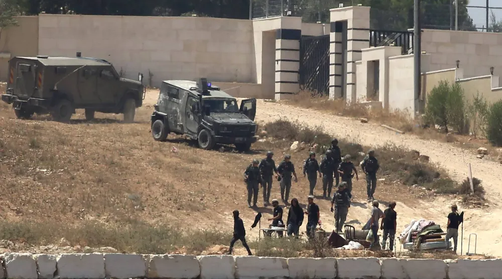 جنود إسرائيليون يقفون حراساً بجوار مستوطنين أمام منازل فلسطينية حاصروها في قرية قصرة جنوب نابلس بالضفة الغربية المحتلة (أ.ب)