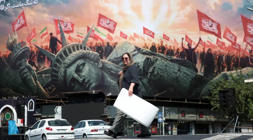 An Iranian woman walks next to an anti-US billboard at the Enghelab square in central Tehran, Iran, 13 August 2026. Tensions between Iran and the US remain high as opposing claims persist over shipping control in the Strait of Hormuz.  EPA/ABEDIN TAHERKENAREH 