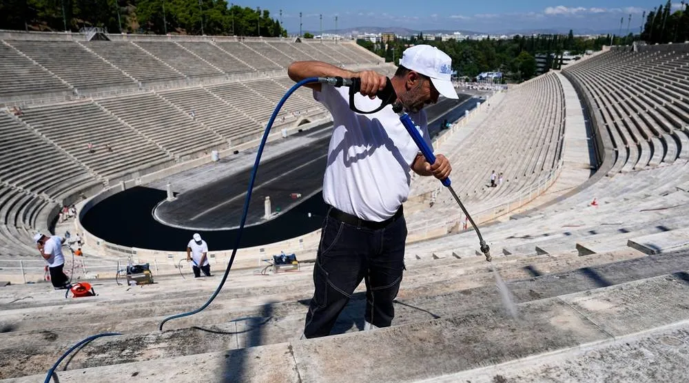 A worker cleans the marble surfaces of the Panathenaic Stadium, also known as "Kallimarmaro," or beautiful marble, which hosted the first modern Olympic Games in 1896, using a high-pressure water hose during renovation work in Athens, Greece, Thursday, Aug. 13, 2026. (AP Photo/Thanassis Stavrakis) 