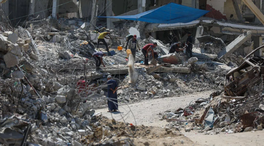 فلسطينيون يستخرجون المعادن من أنقاض المنازل المدمرة في خان يونس لإعادة استخدامها في صنع الخيام بغزة (د.ب.أ)