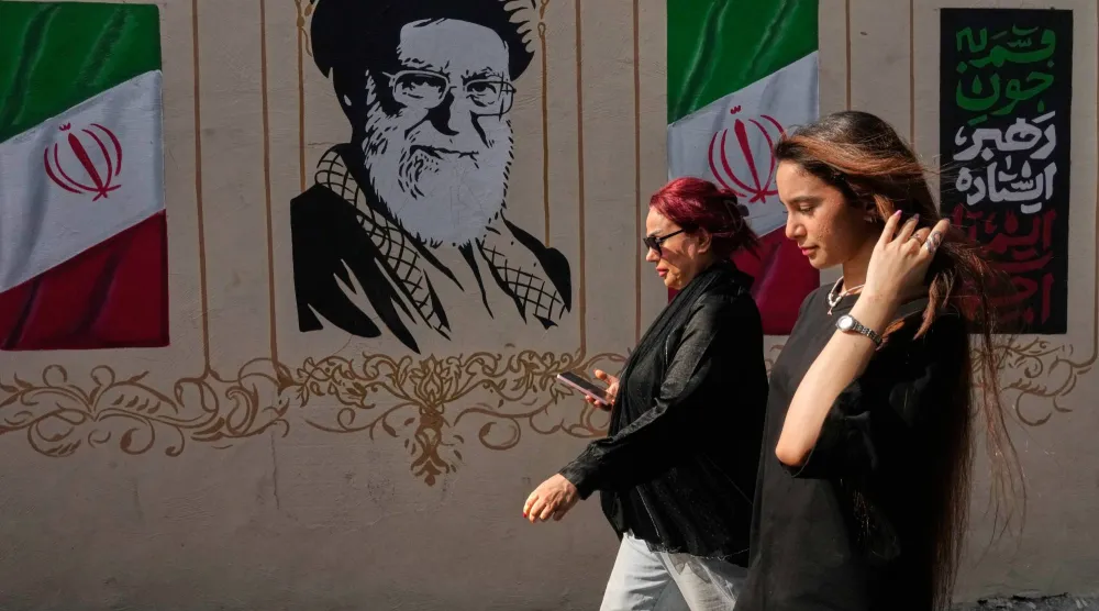إيرانيتان تمران قرب صورة للمرشد الإيراني السابق علي خامنئي، الذي قُتل في الضربات الأميركية - الإسرائيلية في 28 فبراير، وأعلام إيرانية وسط طهران 20 أغسطس 2026 (أ.ب)