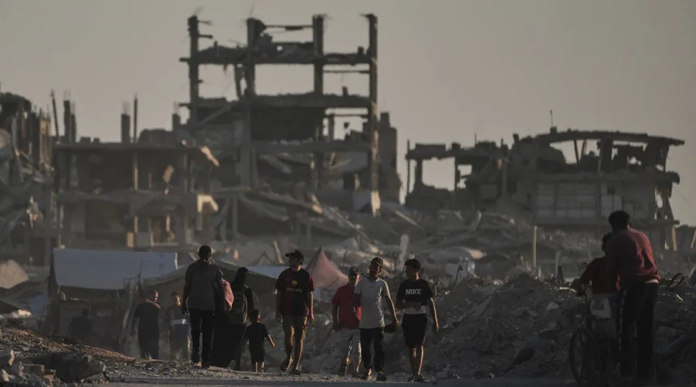 فلسطينيون يمشون وسط المباني المدمرة جراء الضربات الإسرائيلية على قطاع غزة (أ.ب)