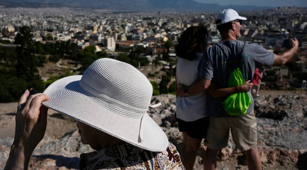 Tourists wearing hats take photographs on the rocky Areios Pagos Hill next to the Acropolis in Athens, Greece, Friday, Aug. 14, 2026. (AP Photo/Thanassis Stavrakis)